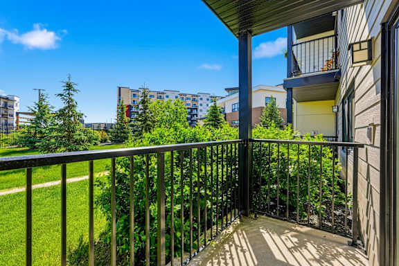 A balcony with a metal railing overlooks a green lawn and apartment buildings.
