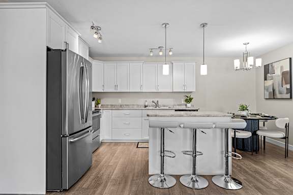 A modern kitchen with a refrigerator, bar stools, and a dining table.