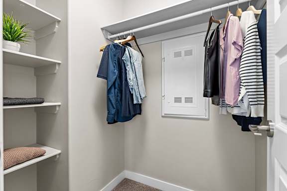 A white closet with clothes hanging and shelves with items.