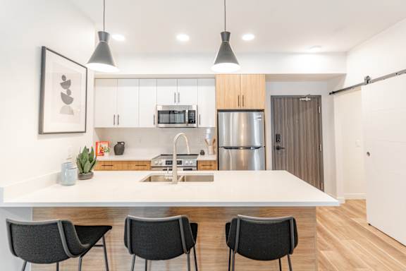 A modern kitchen with a white countertop and black chairs.