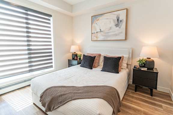 A bedroom with a large bed, two lamps, and a painting on the wall.