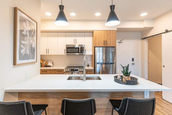 A modern kitchen with a white countertop and black chairs.