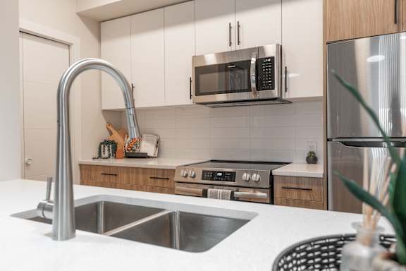 A modern kitchen with a stainless steel sink and a microwave above the stove.at Vista Apartments at Edgemont, Edmonton Alberta