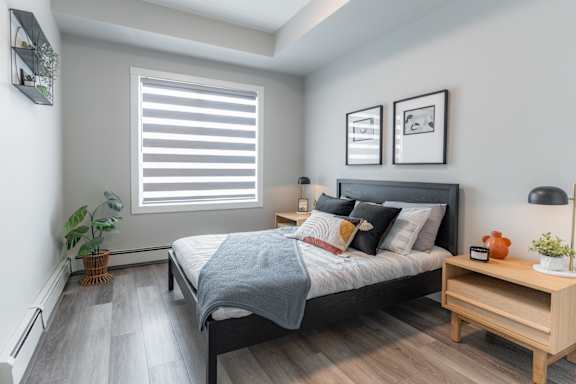 A bedroom with a bed, nightstand, and a window with blinds.