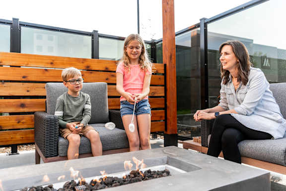 A woman and two children are sitting on a patio with a fire pit at The Artisan at Rangeview, Alberta, T3S 0C4