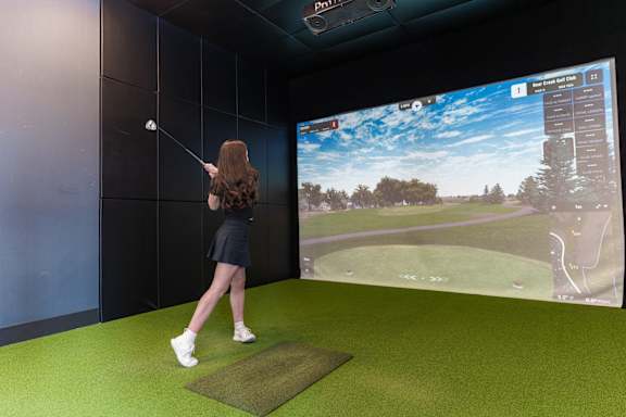 A woman is playing golf in a room with a large screen showing a golf course.