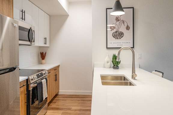 A modern kitchen with a stainless steel refrigerator, wooden cabinets, and a white countertop.at The Artisan at Rangeview, Calgary, Alberta