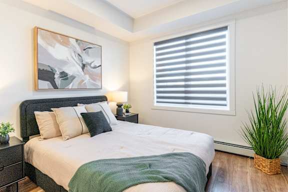 A bedroom with a large bed and a painting on the wall.at The Artisan at Rangeview, Calgary, Alberta