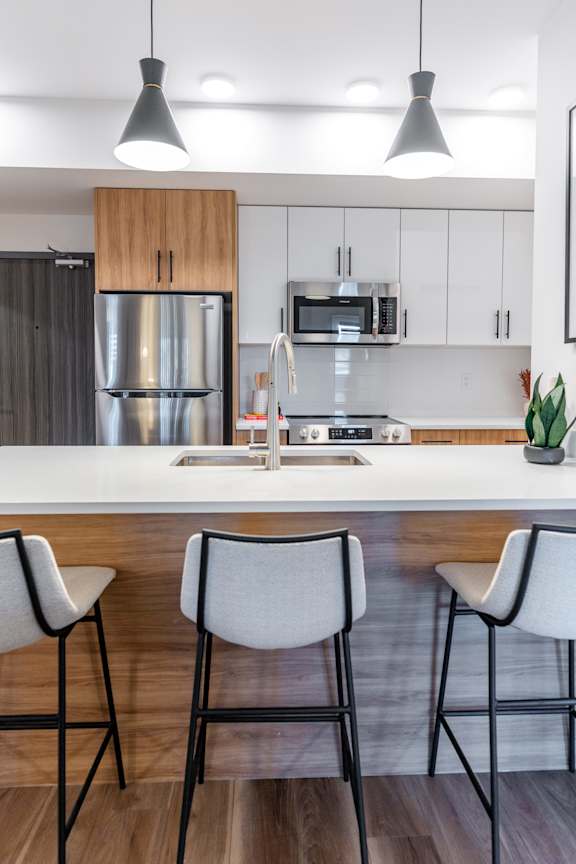A kitchen with a white countertop and bar stools.at The Artisan at Rangeview, Calgary, Alberta