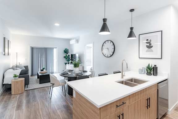 A modern kitchen with a dining table and chairs, a sink, and a clock on the wall.