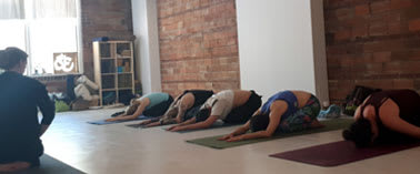 A group of people are practicing yoga in a room with brick walls.