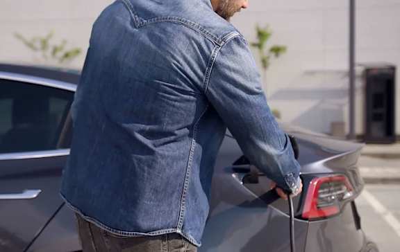 A man in a denim jacket is charging an electric car.