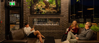 Three people are sitting on a couch in a room with a fireplace.