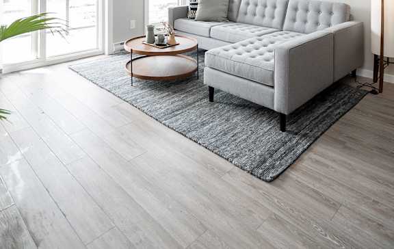 A grey tufted sofa sits on a rug in a room with wooden flooring.
