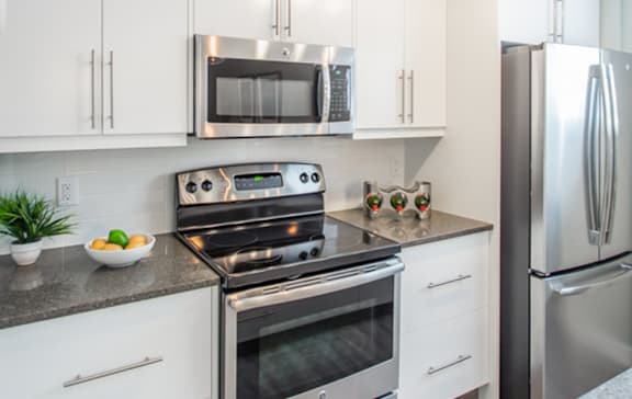 A black refrigerator is in a kitchen with white cabinets.