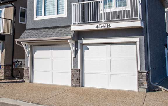 A two-car garage is attached to a gray house.