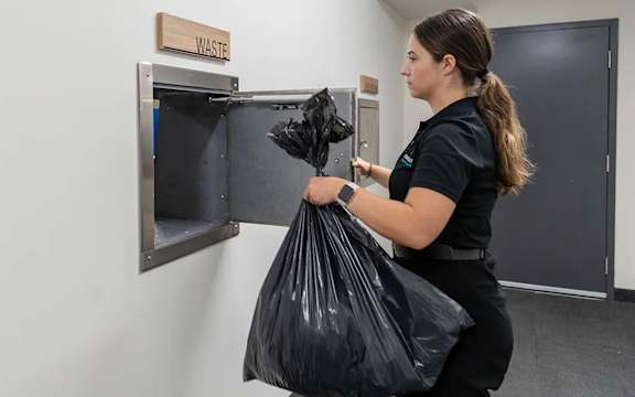 Staff member using waste disposal chute system at Mac and Mullen Apartments, Edmonton, T6R 0S7