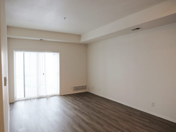 A large empty room with wooden floors and a window with curtains.