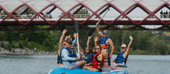 A group of people are riding on a blue watercraft with a red bridge in the background.
