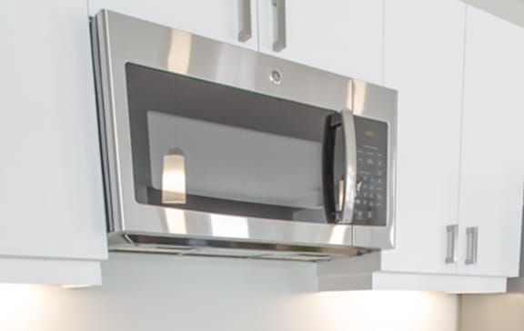 A stainless steel microwave oven with a digital display and control panel is mounted on a wall.