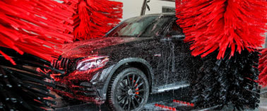 A black car is being washed with red brushes.