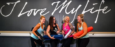 Four women standing in front of a wall that says "I Love My Life".
