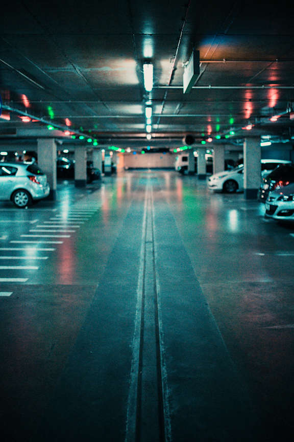 A parking garage with cars parked on both sides and a few cars driving through.at Raymond Block, Edmonton, AB T6E 3R7
