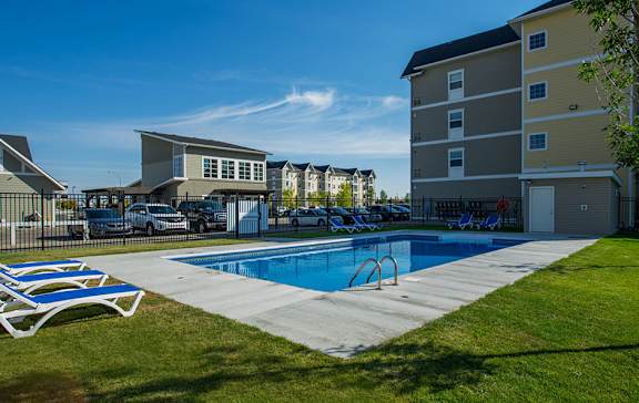 A swimming pool surrounded by a grassy area and apartment buildings.