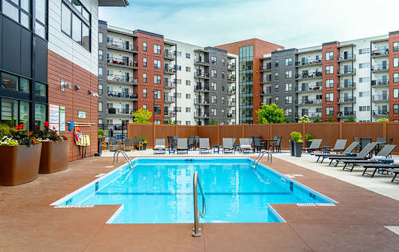 A large swimming pool surrounded by lounge chairs and apartment buildings.