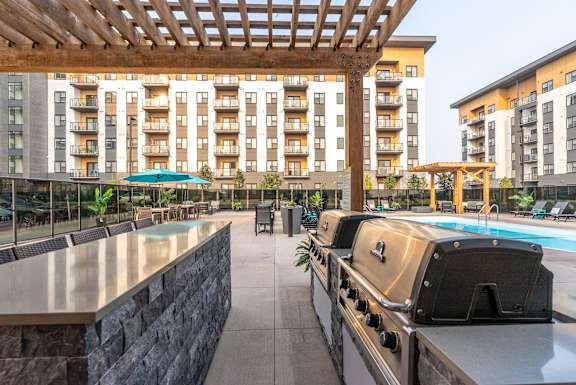 a patio with a grill and a swimming pool at Vibe Apartments at Arbour Lake in Calgary, AB