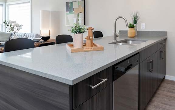 A modern kitchen with a grey countertop and black chairs.