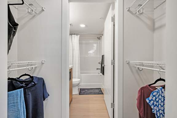 a walk in closet with clothes hanging on the wall and a bathroom in the background at Vista Apartments at Edgemont, Edmonton