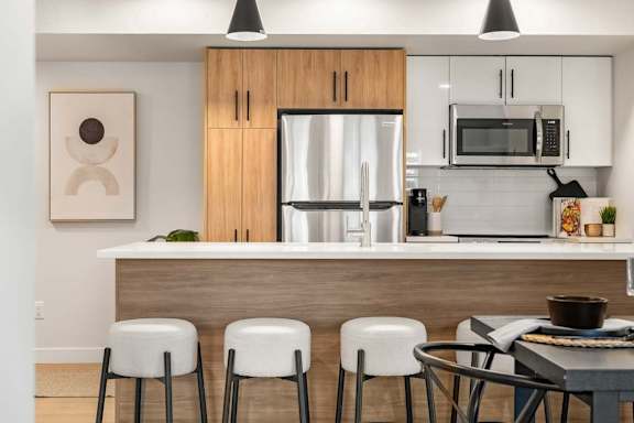 A modern kitchen with a wooden island and white stools.at Skyway Apartments, Alberta