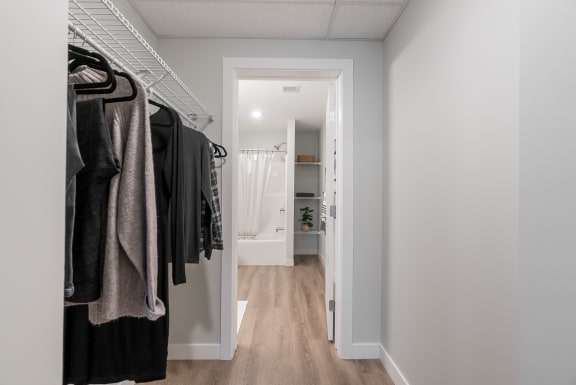 a walk in closet with clothes hanging on a rack and a door to a bathroom at Vibe Apartments at Arbour Lake in Calgary, AB, T3G 4J2