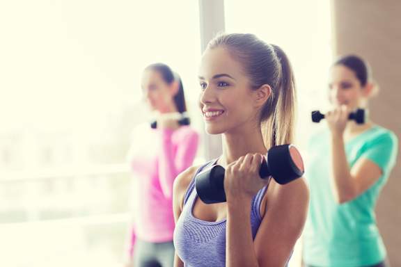 a group of women exercising with dumbbells in a gym at Vibe Apartments at Arbour Lake in Calgary, AB, T3G 4J2
