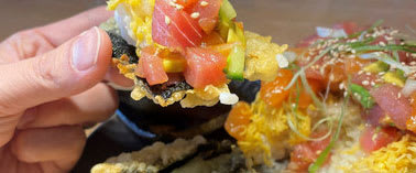 A person is holding a piece of sushi with salmon roe and avocado on top.