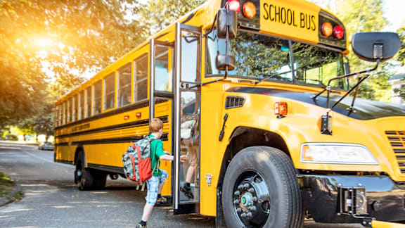 A child is getting off a yellow school bus.