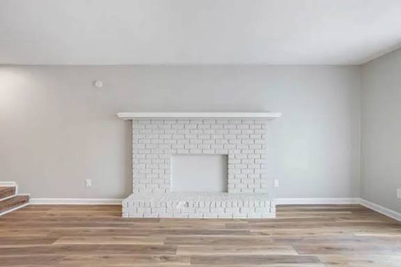 A white brick fireplace in a room with wooden floors at The Onyx Hoover Apartments, Hoover