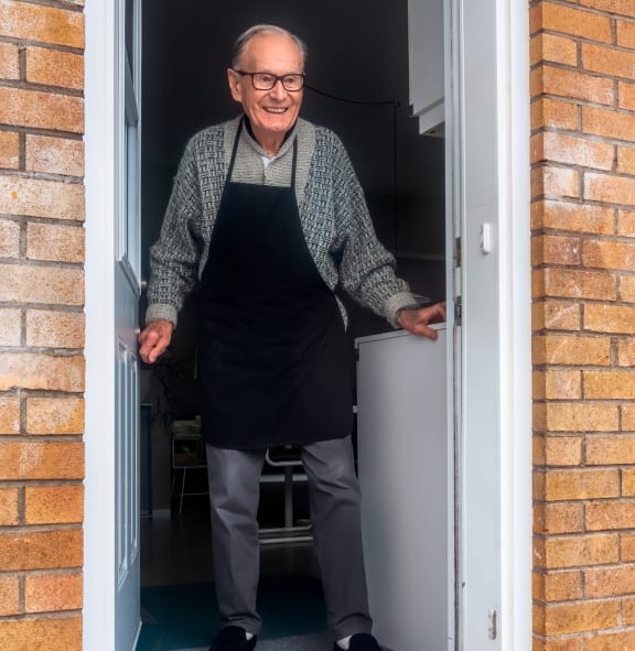 an older man wearing an apron standing in a doorway