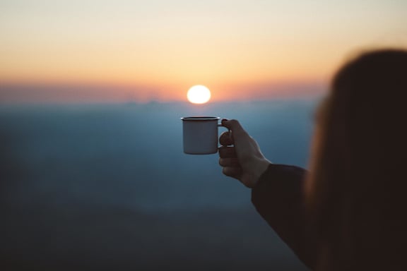 A person holding a mug in front of a sunset.