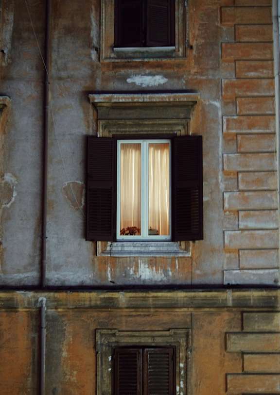 A window with a white curtain and black shutters on a building.