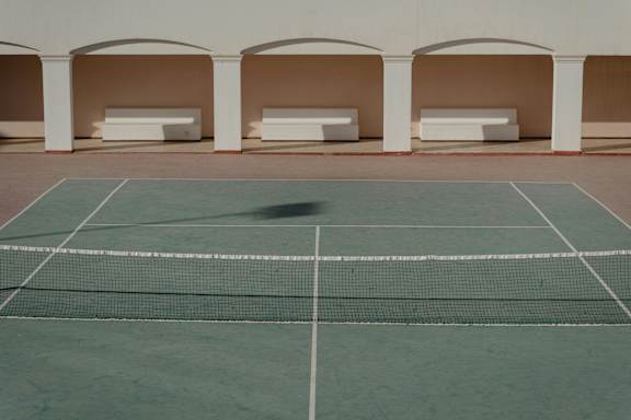A tennis court with a net and white benches under a white building.