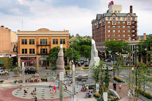 A city square with a monument in the middle and people walking around.
