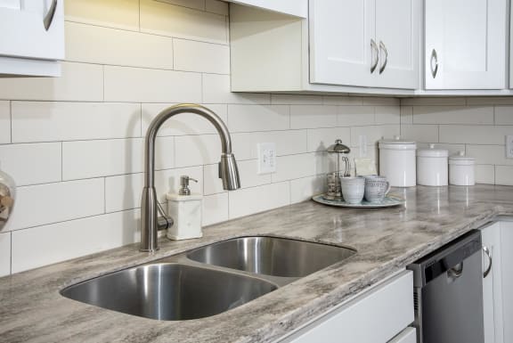 View of sink with detachable sprayer hose complete with sleek stainless steel finishes, granite counter stops, and backsplash tile.
