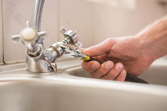 A person is fixing a tap in a sink.