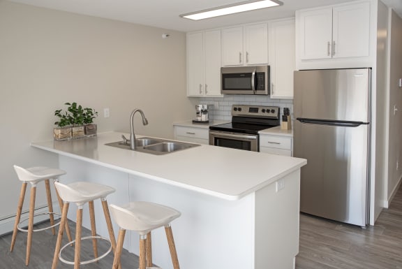 Kitchen with stainless steel appliances, white cabinetry and breakfast bar with sink