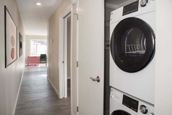 Apartment hallway with open closet, inside is stacked washer and dryer combo