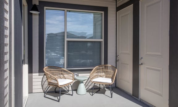 Private balcony with two comfort chairs and door leading inside unit
