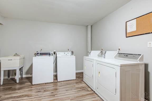 A laundry room with a washer, dryer, ironing board, and sink.