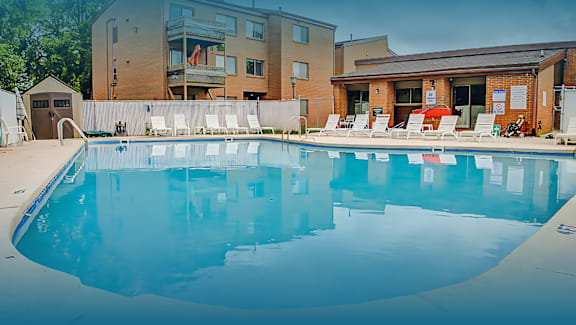 A large swimming pool with lounge chairs and apartment buildings in the background.